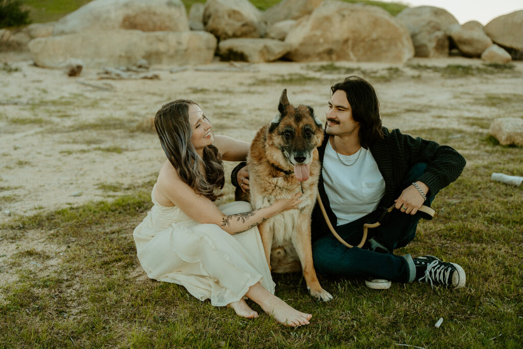 Wedding Photographers Reno capture couple sitting on grass petting pup during engagement photos