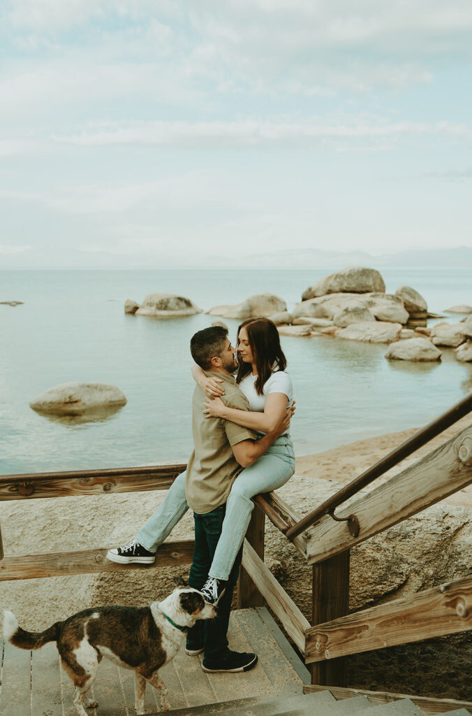 Reno wedding photographer captures couple kissing while woman sits on handrail by beach